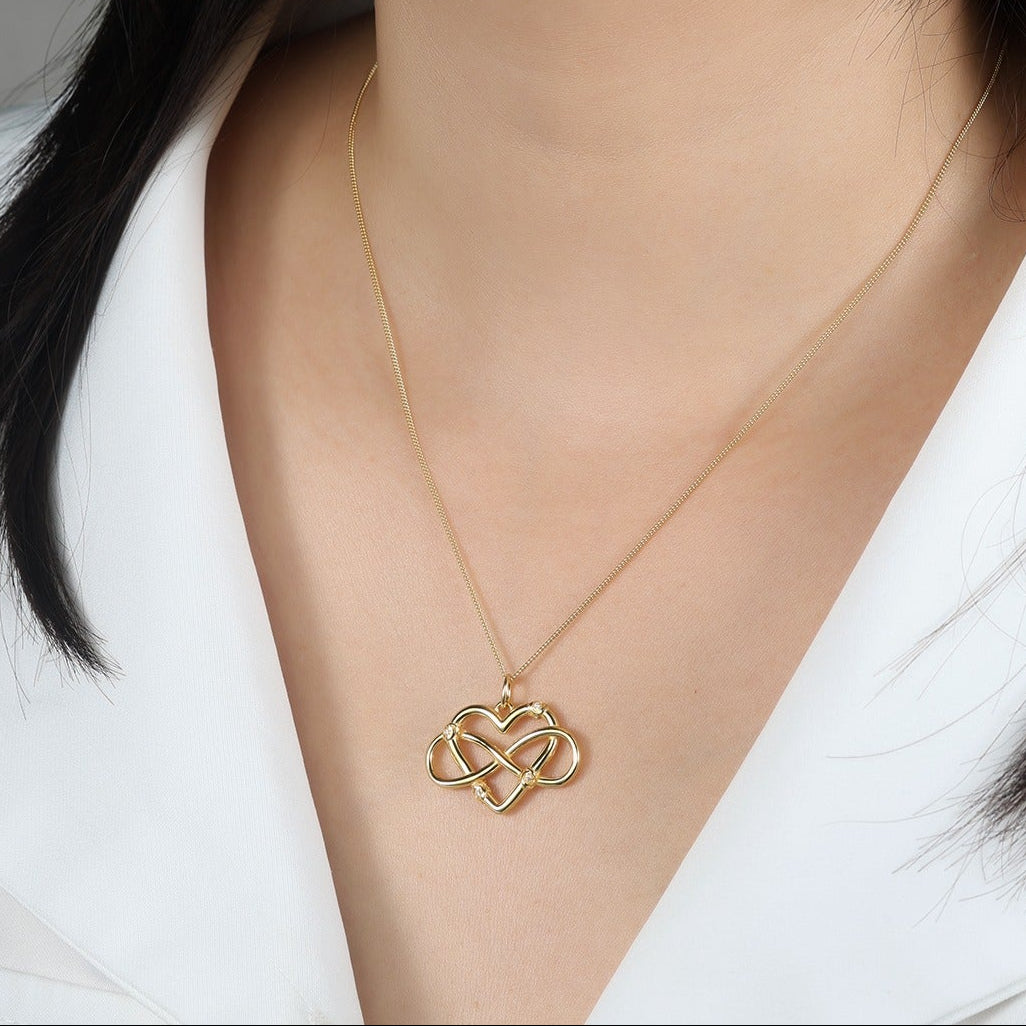 Woman wearing a gold necklace with a heart-shaped pendant against a neutral background
