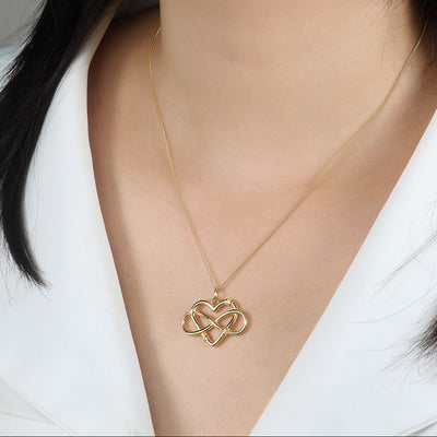 Woman wearing a gold necklace with a heart-shaped pendant against a neutral background