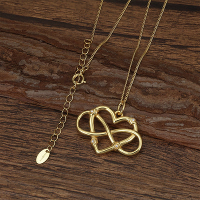 Gold necklace with a heart-shaped and infinity pendant on a wooden surface